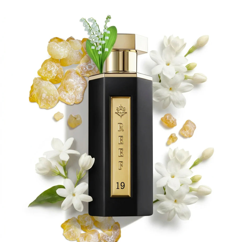 Reef - 19 100ml perfume bottle with gold cap and black body surrounded by white flowers and yellow stones on a white background